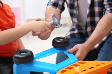 Man and his child as repairman playing with toy cart at home, closeup