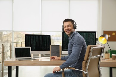 Photo of Happy programmer with headphones working at desk in office