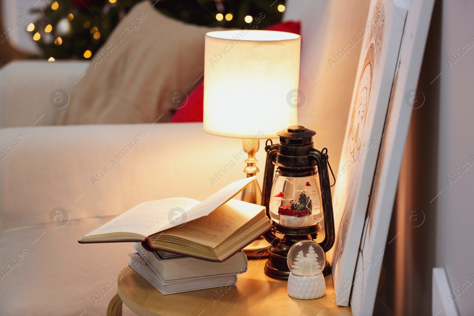 Photo of Books, snowglobes and lamp on wooden table in room. Christmas decor