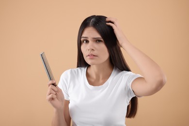 Photo of Emotional woman with comb examining her hair and scalp on beige background. Dandruff problem
