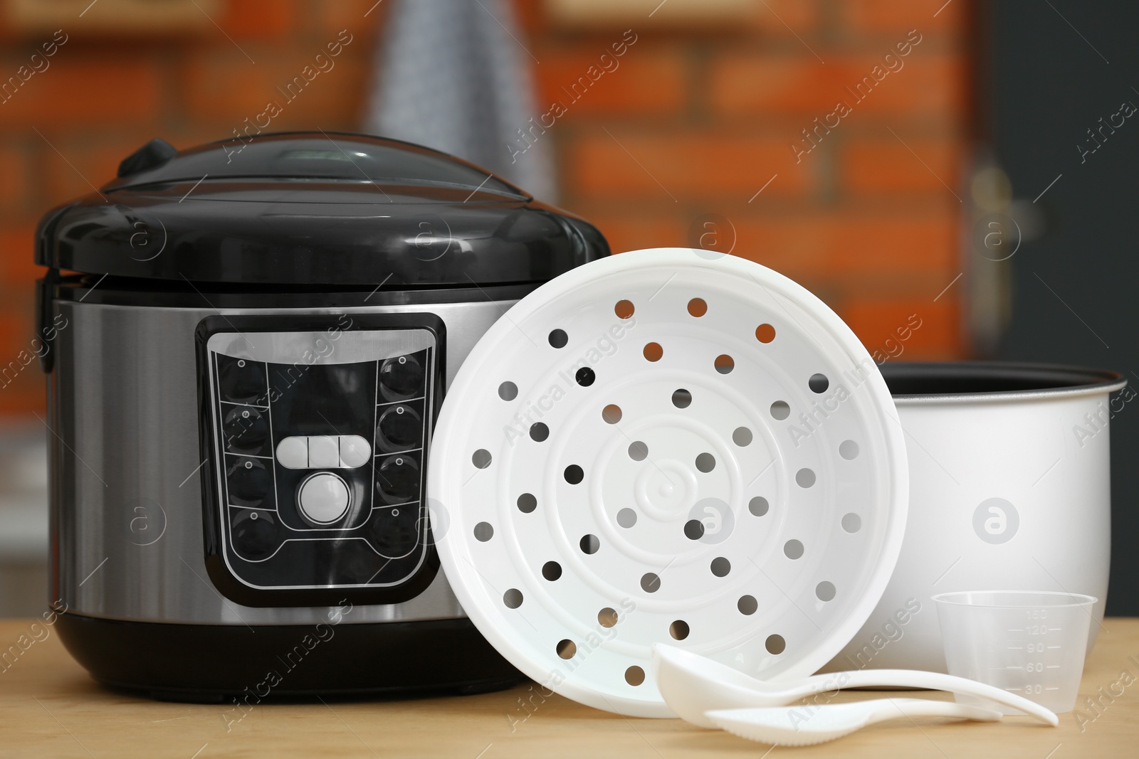 Photo of Modern electric multi cooker, parts and accessories on table in kitchen