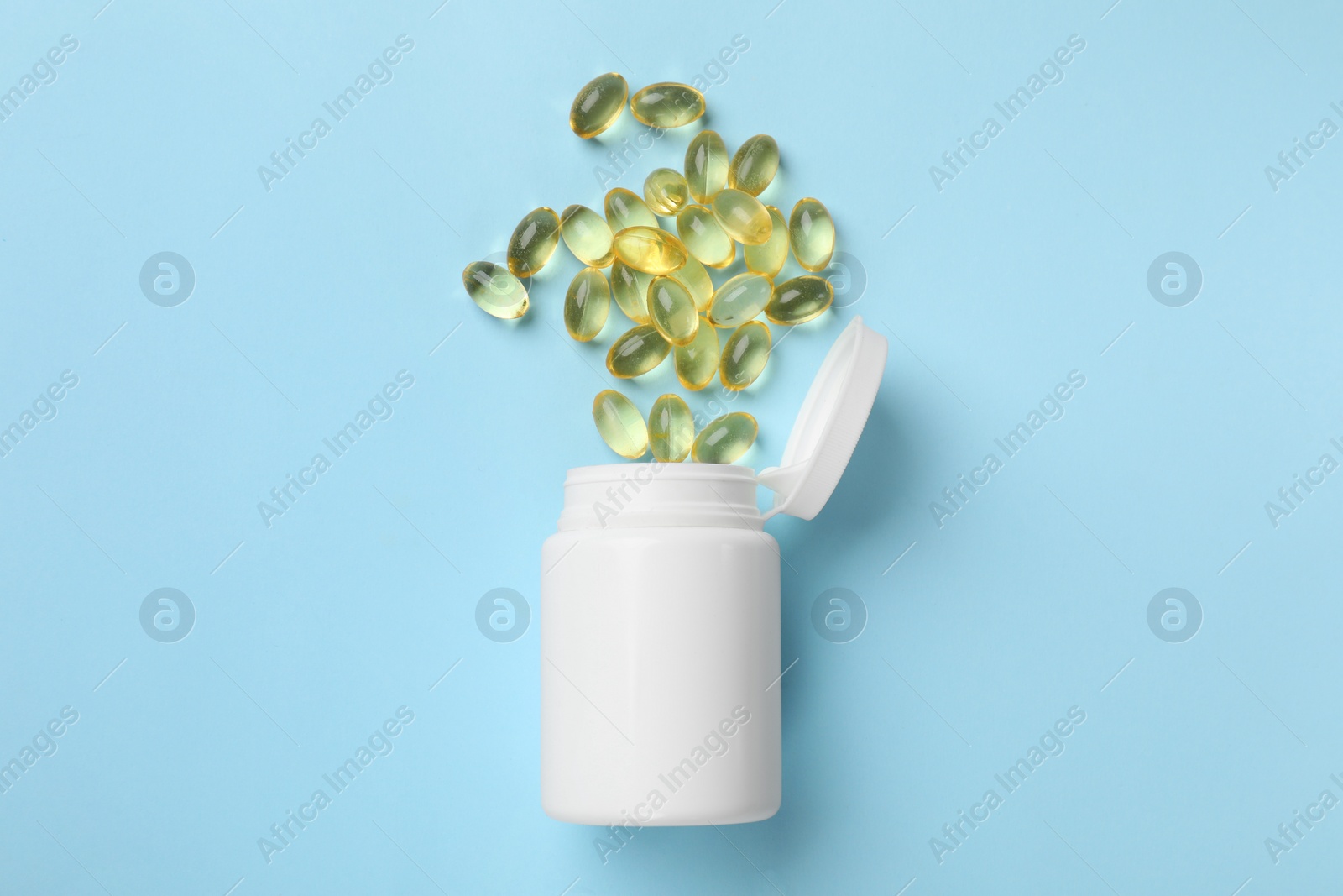 Photo of Vitamin capsules and bottle on light blue background, top view