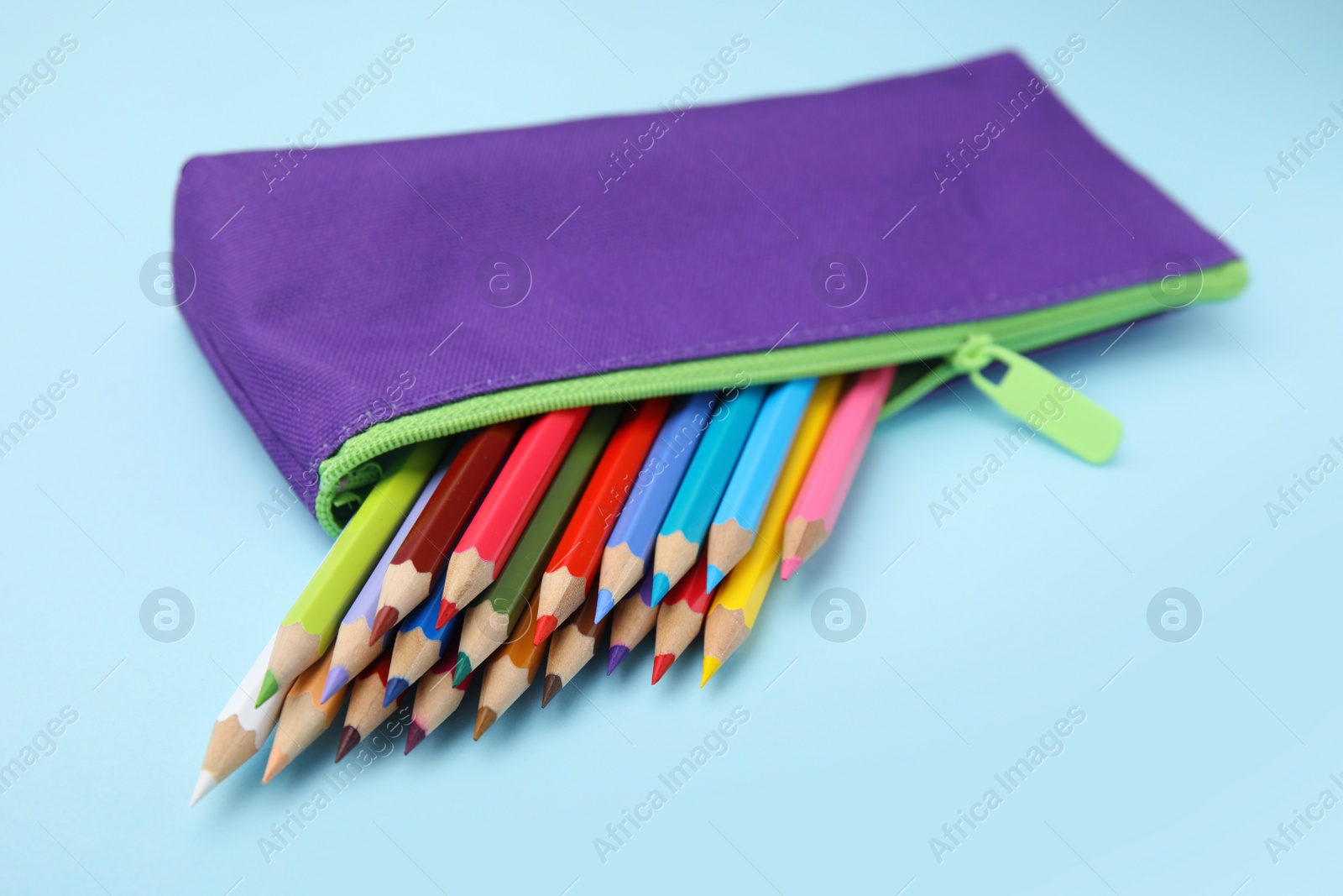 Photo of Many colorful pencils in pencil case on light blue background, closeup