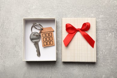 Photo of Key with trinket in gift box on light grey stone background, flat lay. Housewarming party