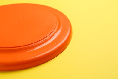 Photo of Orange plastic frisbee disk on yellow background, closeup. Space for text