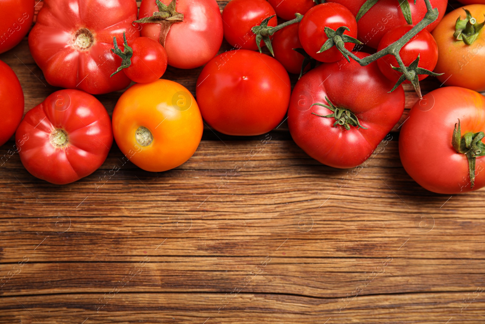 Photo of Many different ripe tomatoes on wooden table, flat lay. Space for text