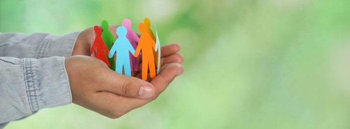 Image of Woman holding paper human figures on blurred green background, closeup view with space for text. Diversity and Inclusion concept