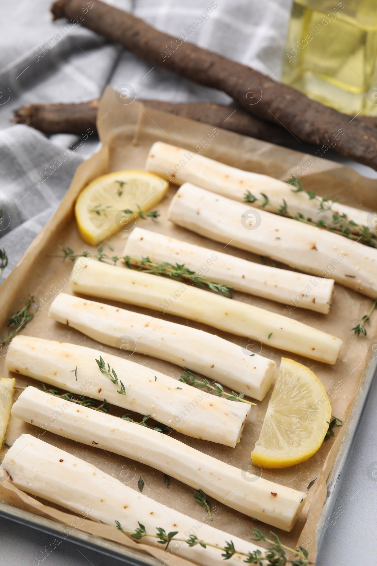 Photo of Baking tray with raw salsify roots, lemon and thyme on white table, closeup