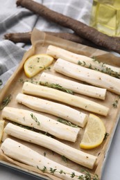 Photo of Baking tray with raw salsify roots, lemon and thyme on white table, closeup