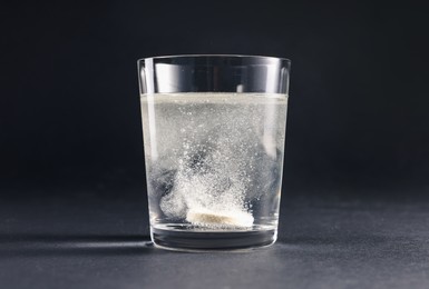 Effervescent pill dissolving in glass of water on grey table