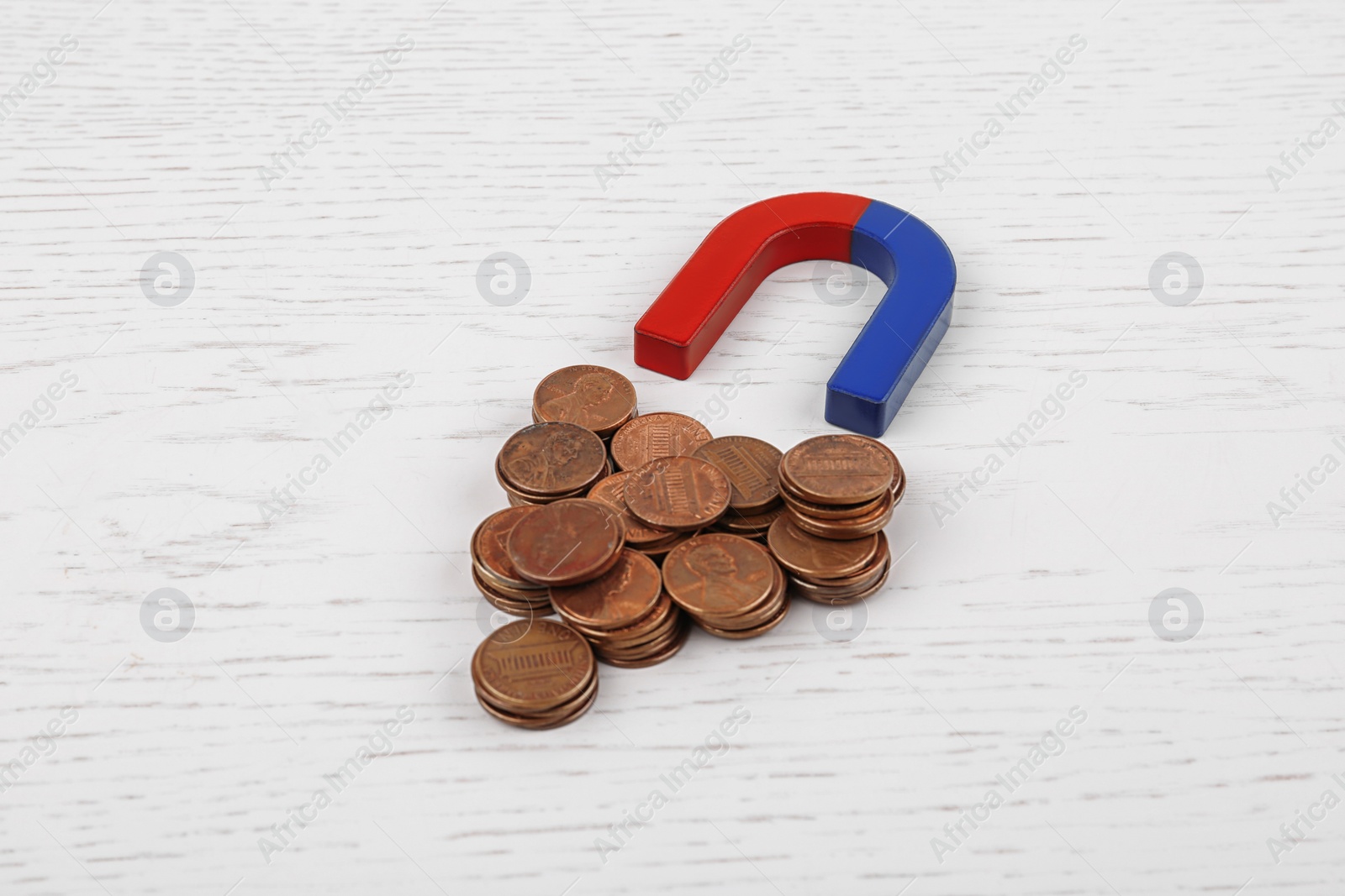 Photo of Magnet attracting coins on white wooden table