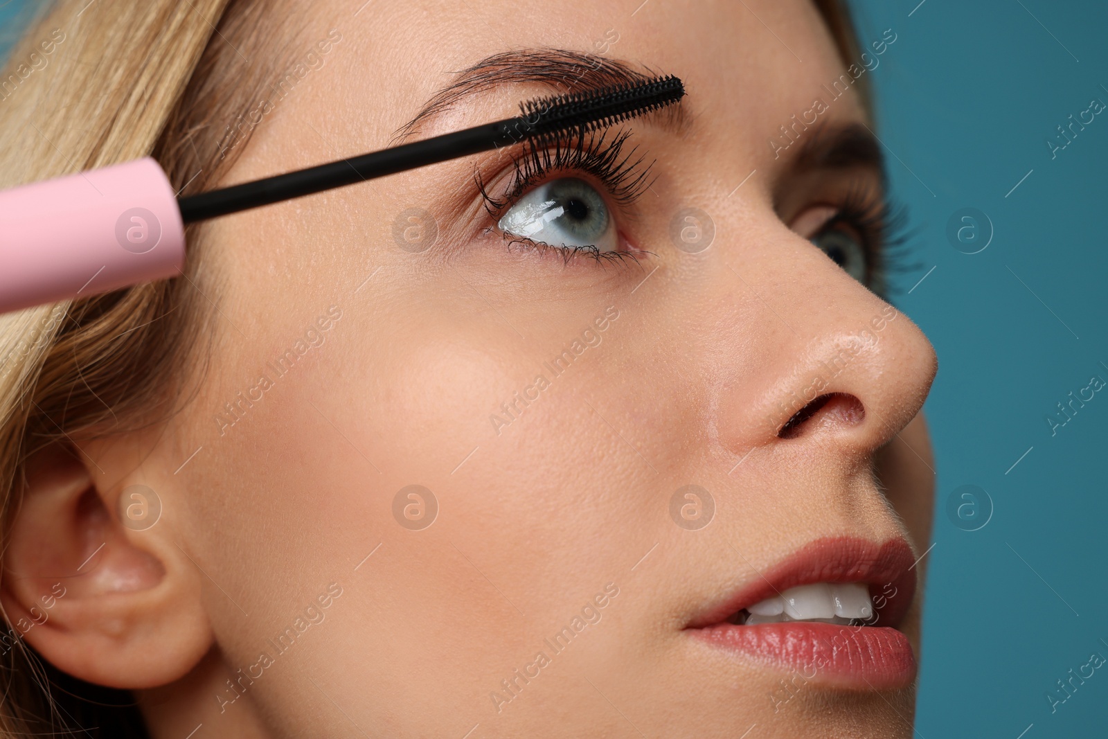 Photo of Beautiful woman applying mascara on light blue background, closeup