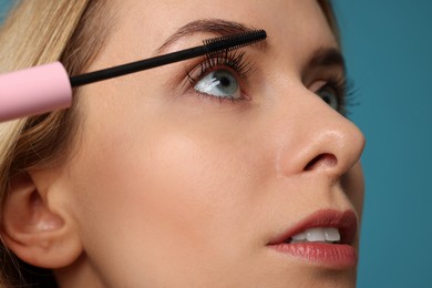 Beautiful woman applying mascara on light blue background, closeup