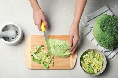 Photo of Woman cutting savoy cabbage on wooden board at table, top view