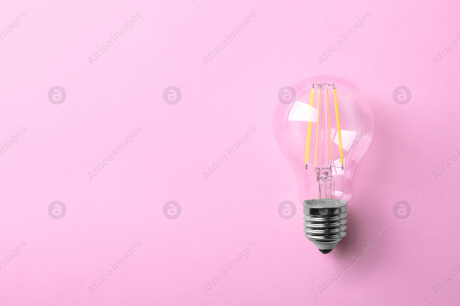 Photo of Vintage filament lamp bulb on pink background, top view. Space for text