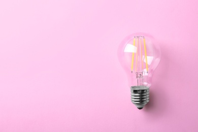 Photo of Vintage filament lamp bulb on pink background, top view. Space for text