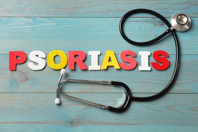 Photo of Word Psoriasis made of paper letters and stethoscope on light blue wooden table, flat lay