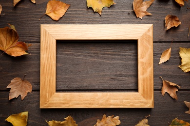 Photo of Flat lay composition with autumn leaves and frame on wooden background. Space for text