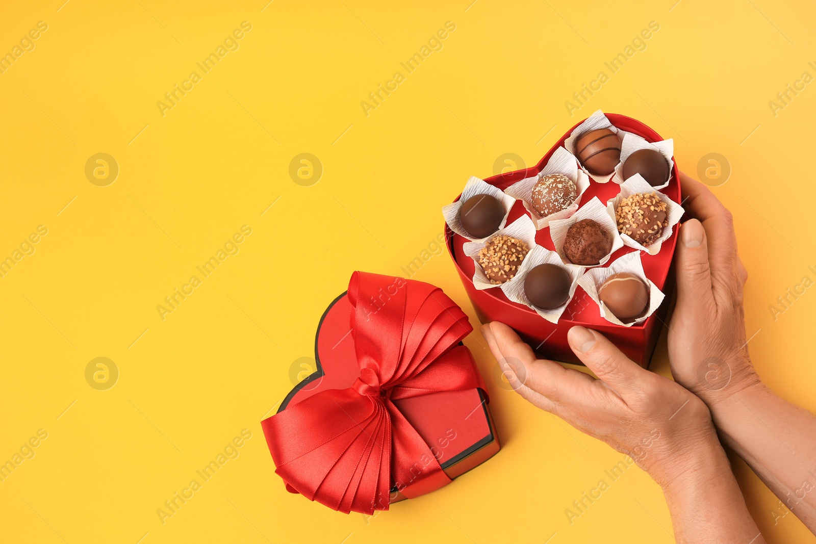 Photo of Woman with heart shaped box of delicious chocolate candies on yellow background, closeup. Space for text