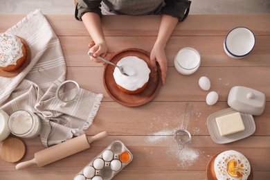 Photo of Young woman decorating traditional Easter cake with glaze at wooden table, top view