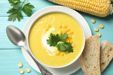 Photo of Delicious creamy corn soup served on turquoise wooden table, flat lay