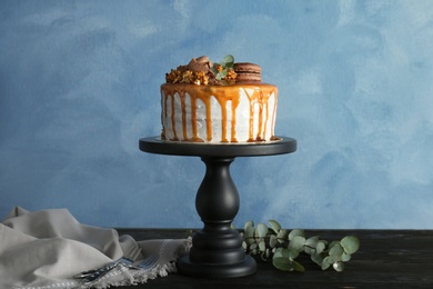 Dessert stand with delicious caramel cake on table against color background