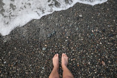 Woman standing on pebble beach near beautiful sea wave outdoors, top view