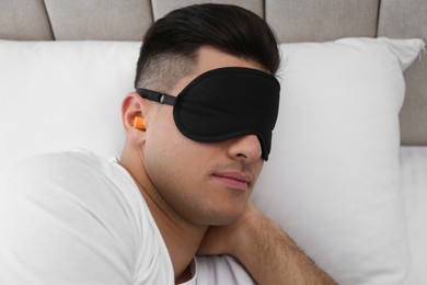 Photo of Man with foam ear plugs and mask sleeping in bed