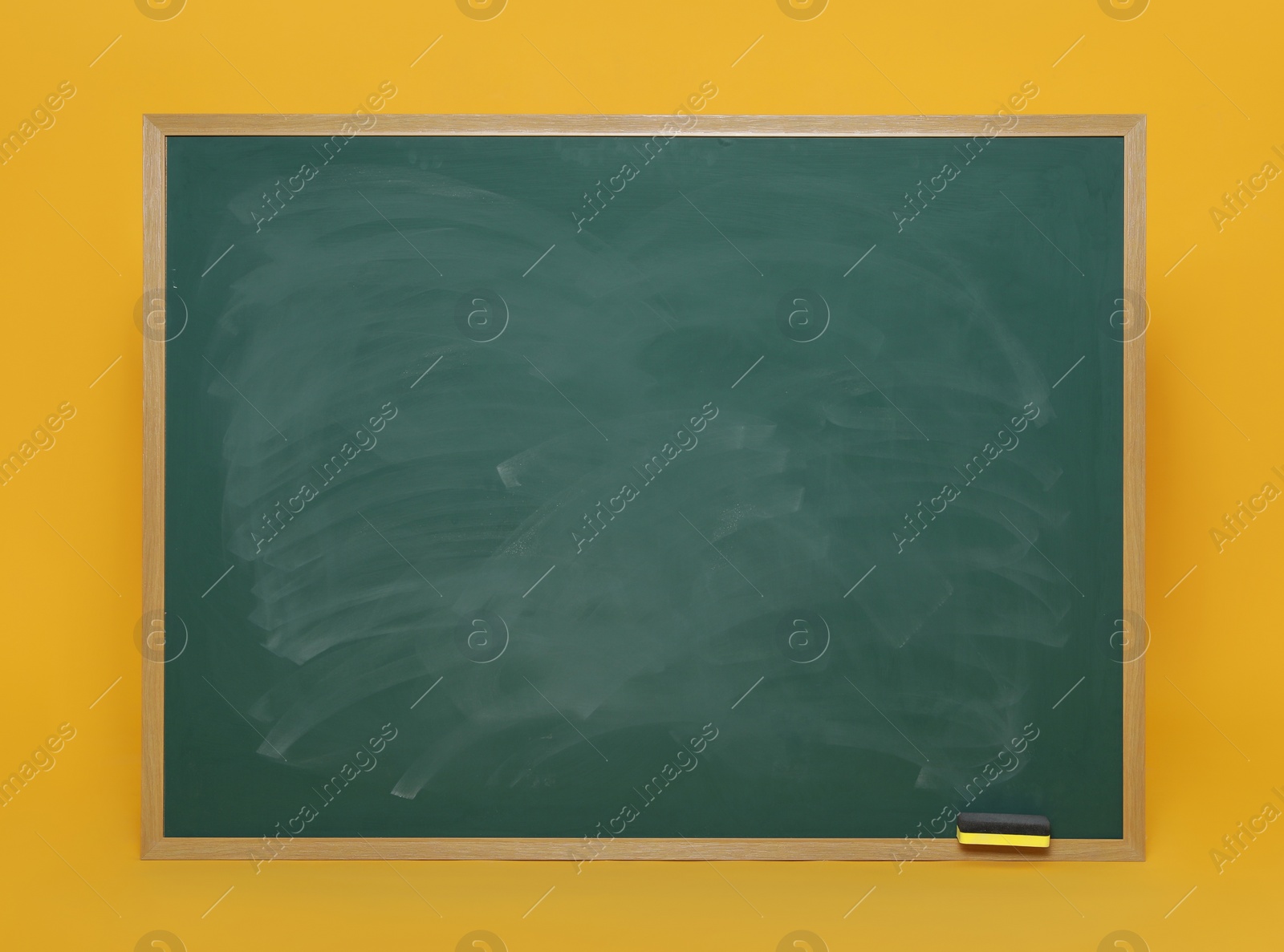 Photo of Dirty green chalkboard with duster on orange background