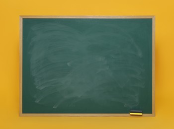 Photo of Dirty green chalkboard with duster on orange background
