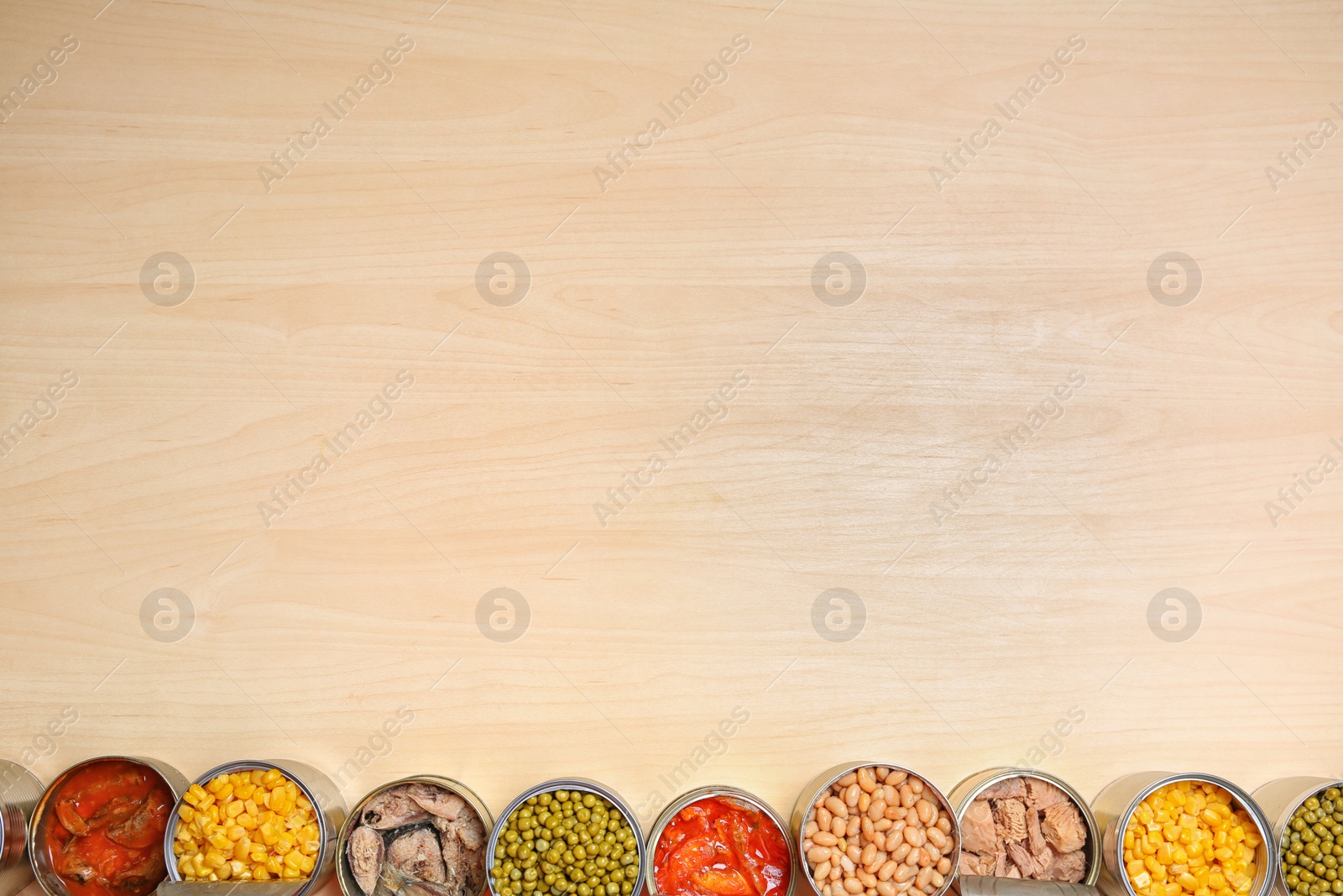 Photo of Open tin cans of conserved products on wooden table, flat lay with space for text