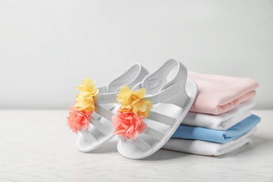 Pair of cute baby sandals and stack of clothes on table