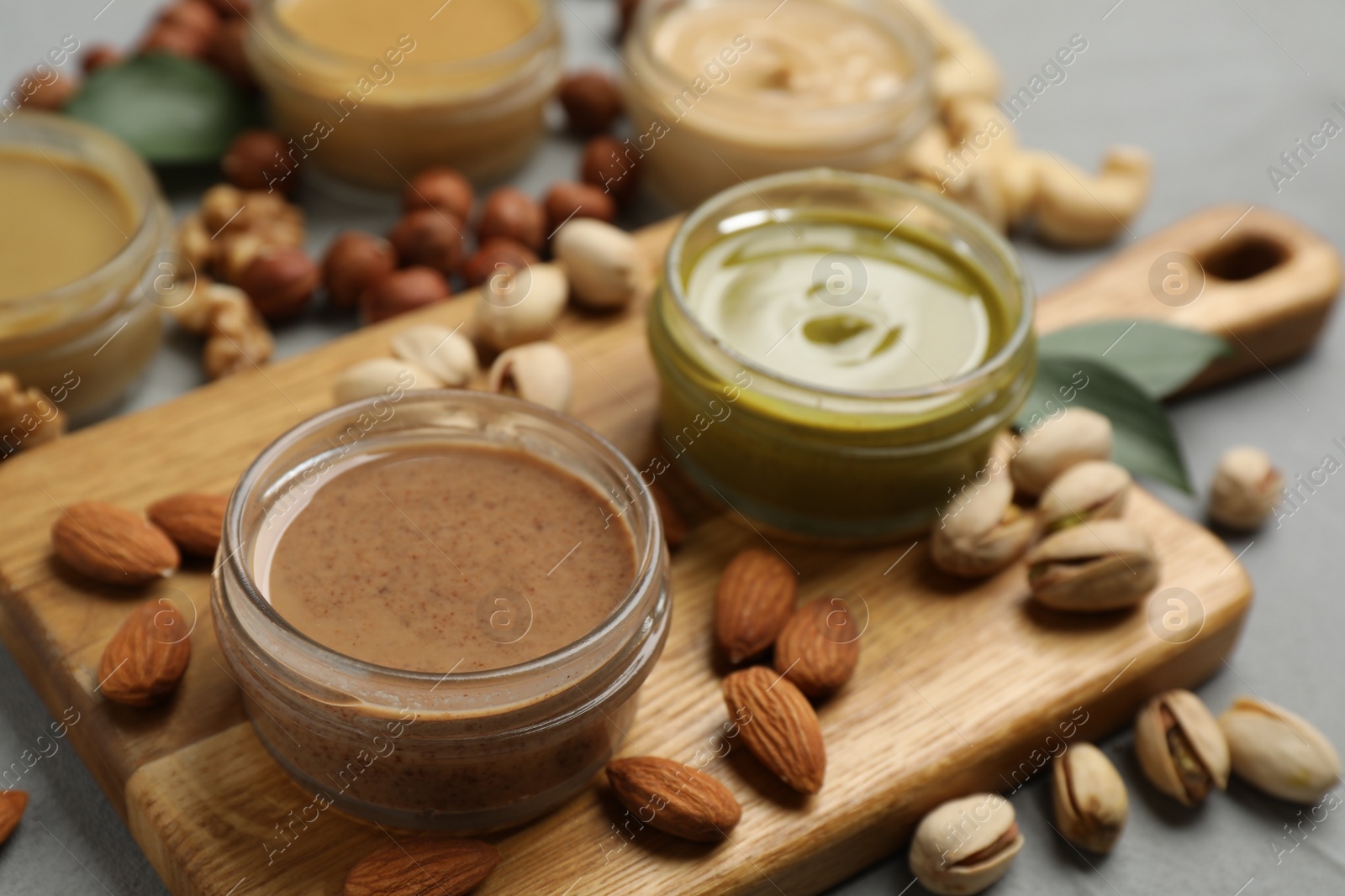 Photo of Jars with butters made of different nuts and ingredients on grey table, closeup