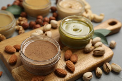 Jars with butters made of different nuts and ingredients on grey table, closeup