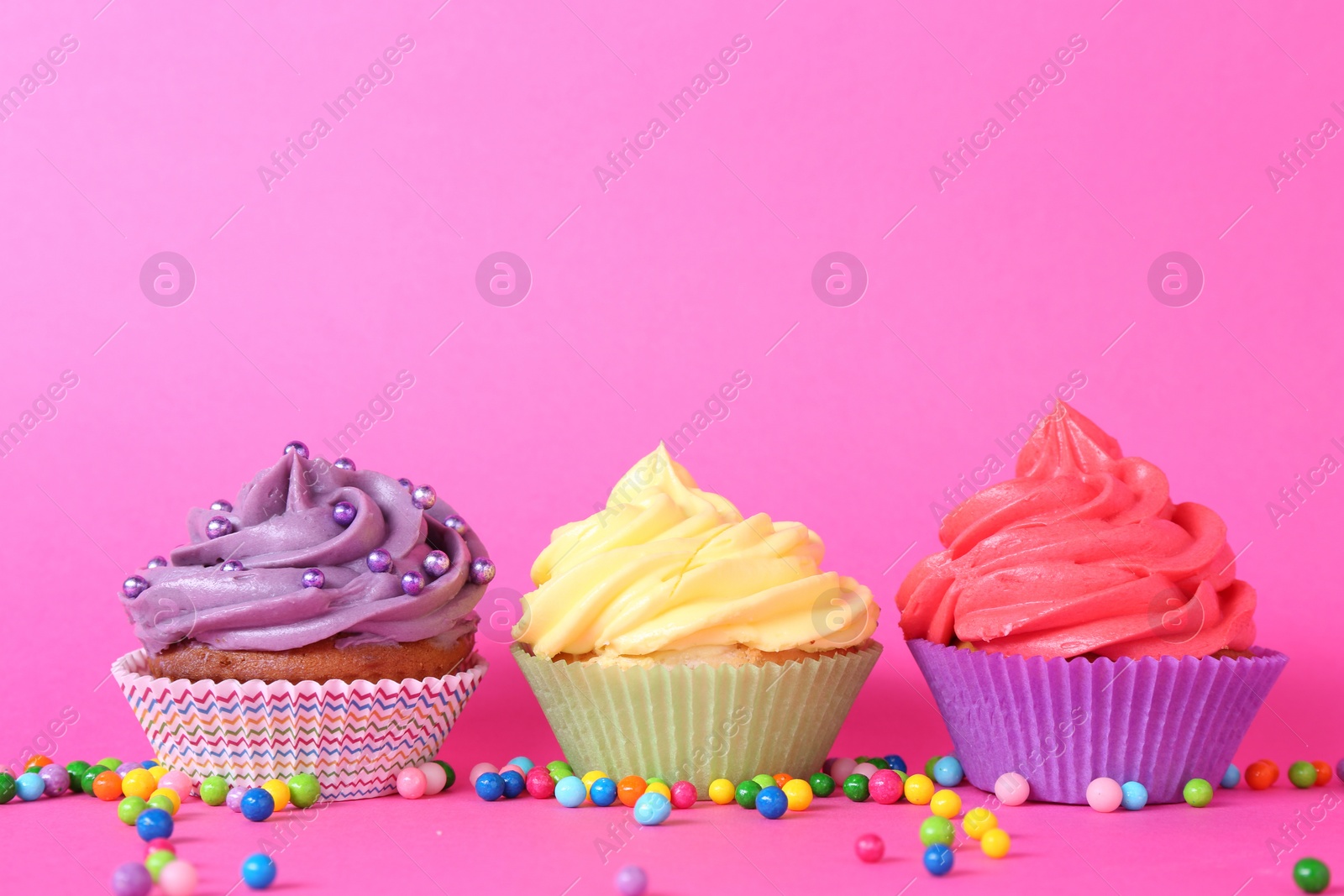 Photo of Delicious cupcakes with bright cream and sprinkles on pink background. Space for text