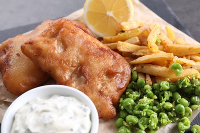 Photo of Tasty fish, chips, sauce and peas on table, closeup