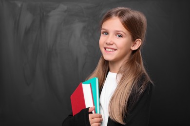 Photo of Smiling schoolgirl with books near blackboard. Space for text
