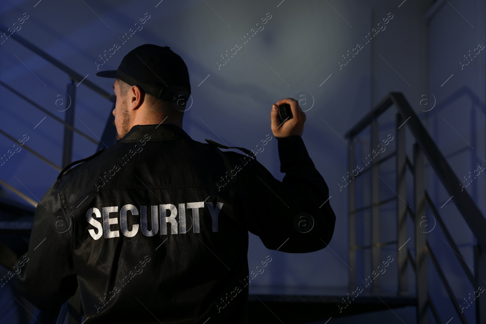 Photo of Male security guard with flashlight going up stairs in darkness