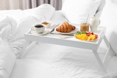 Photo of Wooden tray with tasty breakfast on bed at home