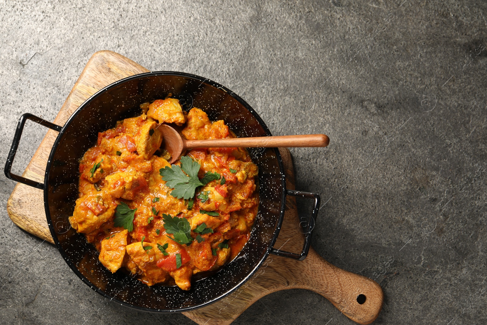 Photo of Delicious chicken curry in frying pan and spoon on grey table, top view. Space for text
