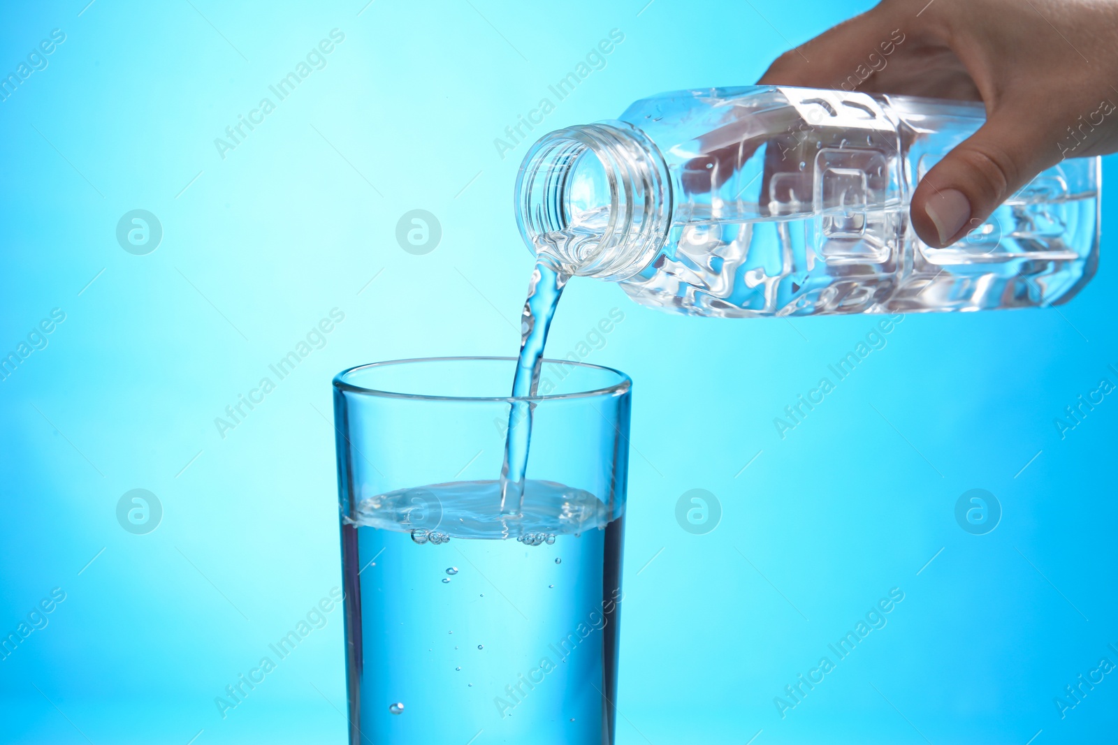 Photo of Woman pouring water from bottle into glass on blue background, closeup