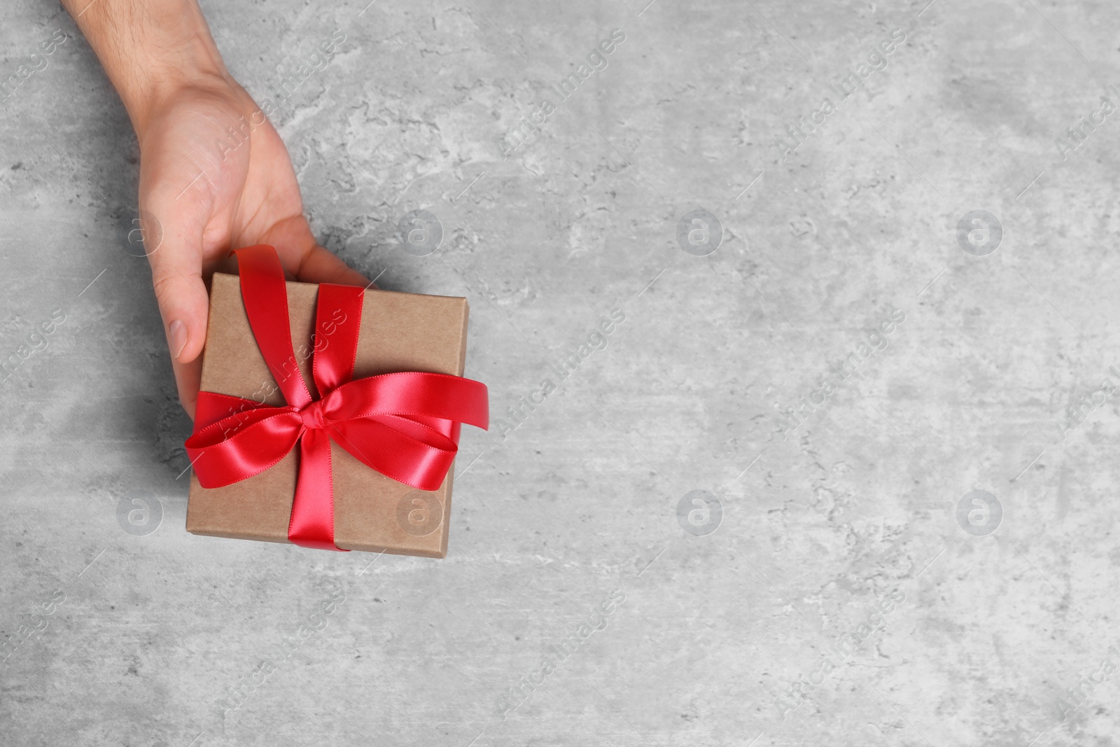 Photo of Man holding gift box with red bow at grey table, top view. Space for text