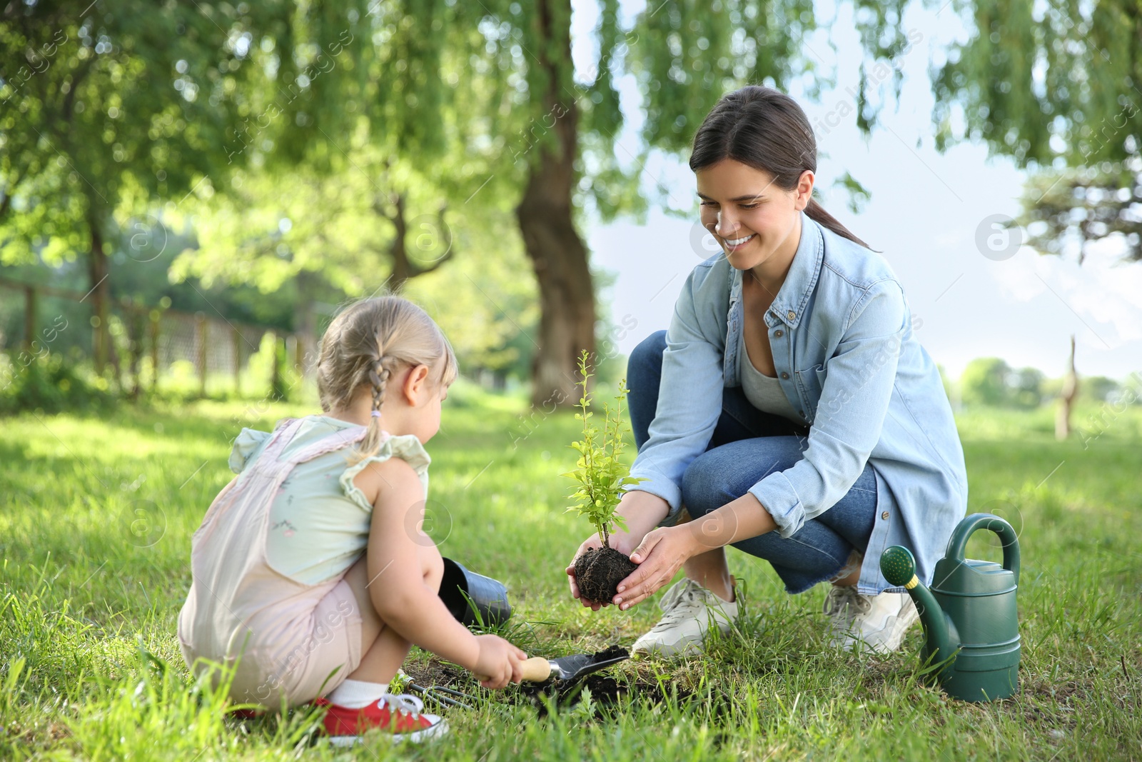 Photo of Mother and her daughter planting tree together in garden