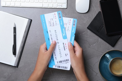 Woman with airline tickets at grey table, top view. Travel agency concept