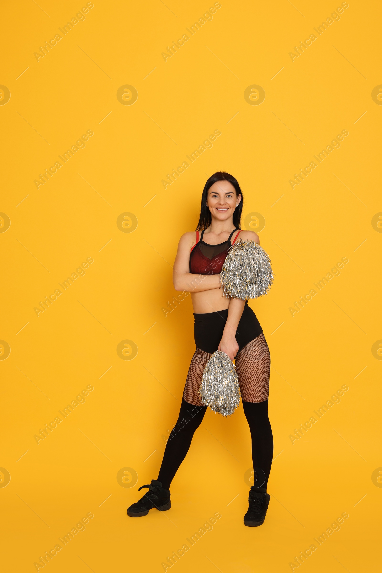 Photo of Beautiful cheerleader in costume holding pom poms on yellow background