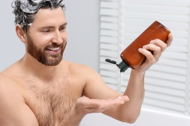 Photo of Happy man pouring shampoo onto his hand in shower