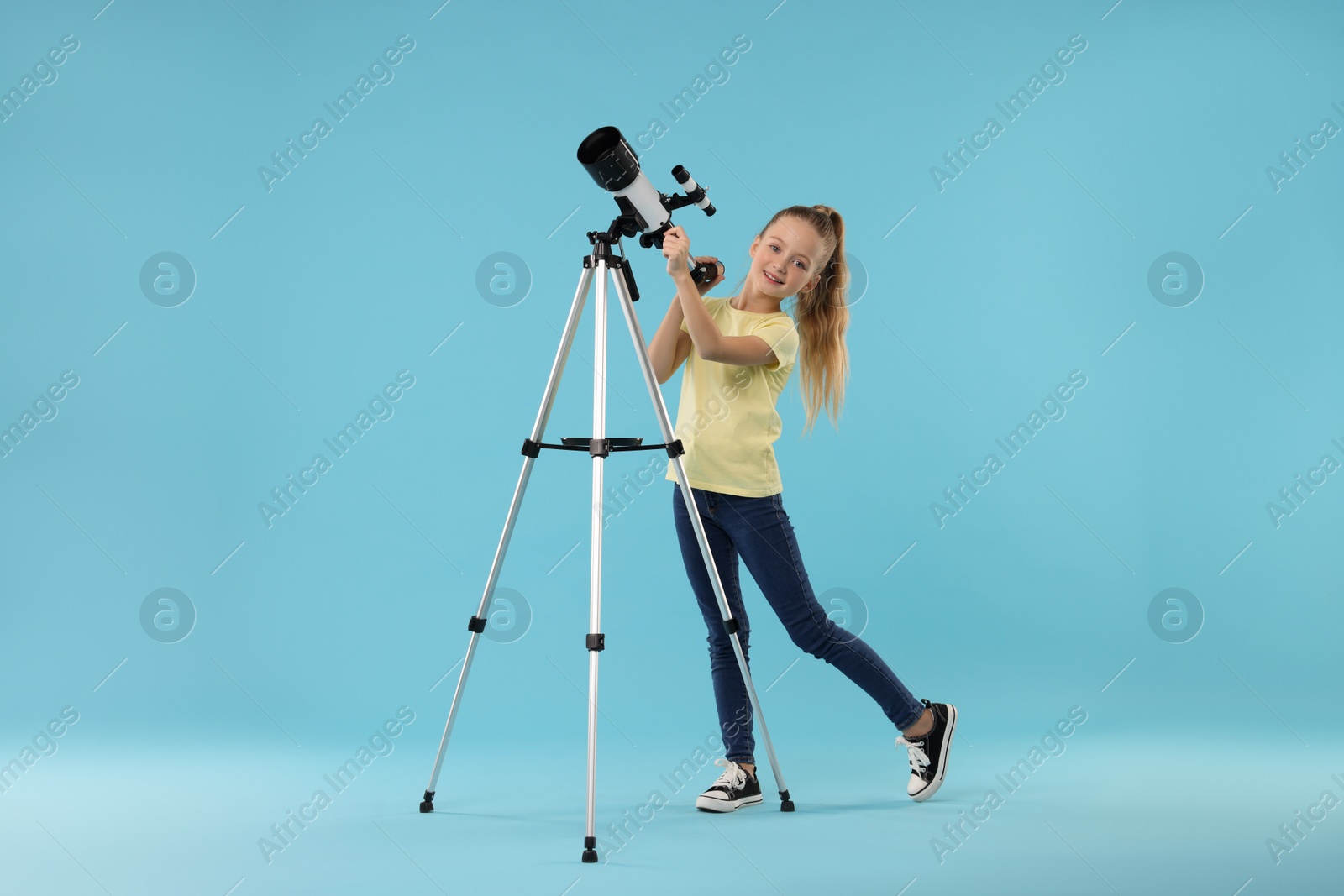 Photo of Happy little girl with telescope on light blue background