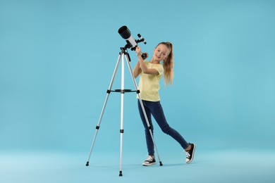 Happy little girl with telescope on light blue background