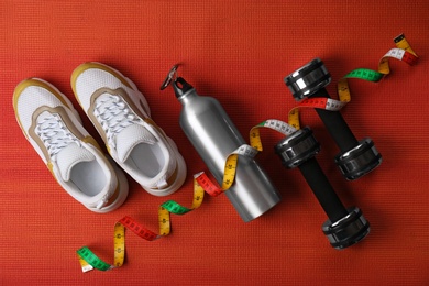 Photo of Flat lay composition of training shoes, dumbbells, bottle and measuring tape on color background