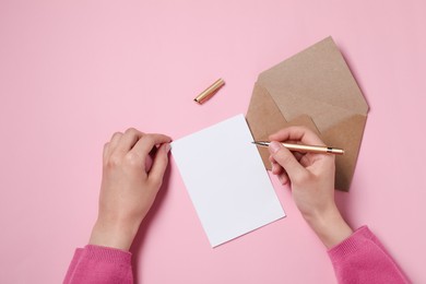 Woman writing letter at pink table, top view. Space for text